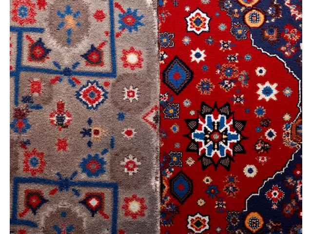 Alfombra persa de intrincados diseños y colores vibrantes, recién limpiada y desodorizada, con las fibras visiblemente levantadas y sucias, contrastando con una zona de la alfombra ya tratada, limpia, nítida y con sus colores originales restaurados. La imagen captura el delicado proceso con un enfoque en la eliminación de suciedad y la revitalización de la fibra.