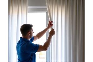 Un operario de Hilos Limpios instala una cortina limpia y planchada en el riel de una ventana, con las cortinas ya colgadas y cayendo perfectamente, mostrando el resultado final de un trabajo detallado y profesional que da impecabilidad al hogar u oficina.
